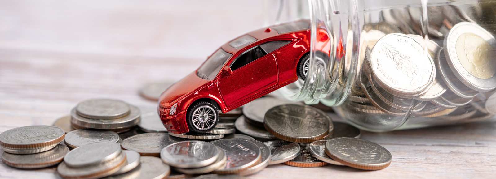 Voiture miniature rouge sortant d'un bocal rempli de pièces représentant des économies sur l'assurance auto électrique.