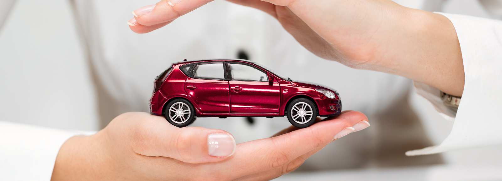 Voiture rouge miniature protégée entre deux mains symbolisant l'assurance auto et la sécurité